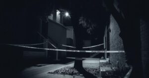 A dark alley at night with police tape, a silhouette of two trees, and scattered leaves, conveying a sense of danger.